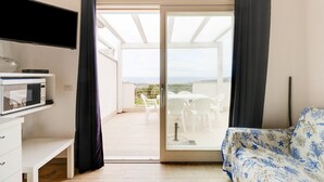 A room with a bed, a TV, a microwave, a bench, and a sliding glass door leading to an outdoor area with a table and chairs. - Terrazza, air conditioning and post bus private (Paduledda)