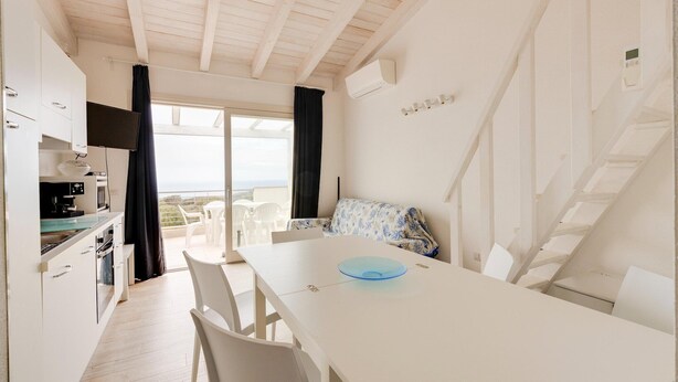 A modern kitchen with white cabinets, a dining area with a white table and chairs, a sofa with a floral pattern, and a staircase leading to an upper level. - Terrazza, air conditioning and post bus private (Paduledda)