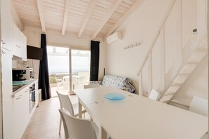 A modern kitchen with white cabinets, a dining area with a white table and chairs, a sofa with a floral pattern, and a staircase leading to an upper level. - Terrazza, air conditioning and post bus private (Paduledda)
