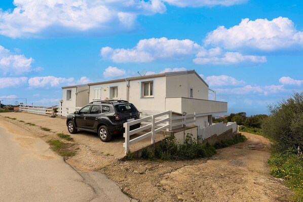 A two-story building with a white exterior, a parked SUV, and a white fence leading to the entrance. - Terrazza, air conditioning and post bus private (Paduledda)