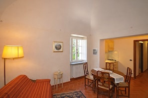 Ein gemütliches Zimmer mit Bett, einem kleinen Tisch, Stühlen, einer Lampe, einem Fenster und einer Küchenzeile.