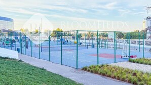 A basketball court with a fence, surrounded by grass and a paved walkway. - Bloomfields 1br Deluxe in Water Edge (Abu Dhabi)