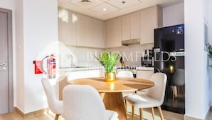 A modern kitchen with a round dining table, white chairs, and a black refrigerator. - Bloomfields 1br Deluxe in Water Edge (Abu Dhabi)