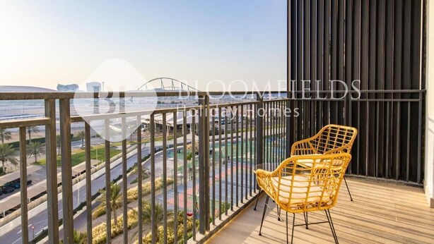 A balcony with a view of a road and greenery, a yellow chair, and a dark vertical panel. - Bloomfields 1br Deluxe in Water Edge (Abu Dhabi)
