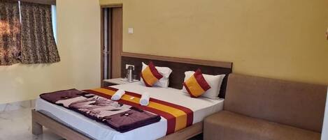 A hotel room with a bed, a sofa, a window with curtains, and an air conditioning unit.