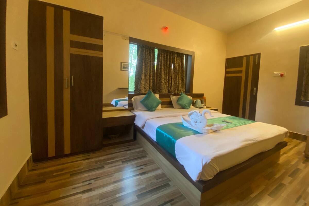 A hotel room with a large bed, a wooden wardrobe, a bedside table with a lamp, and a window with curtains.