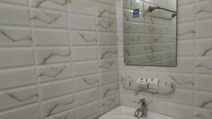 A bathroom with white marble tiles, a white sink, a mirror, and a soap dispenser.