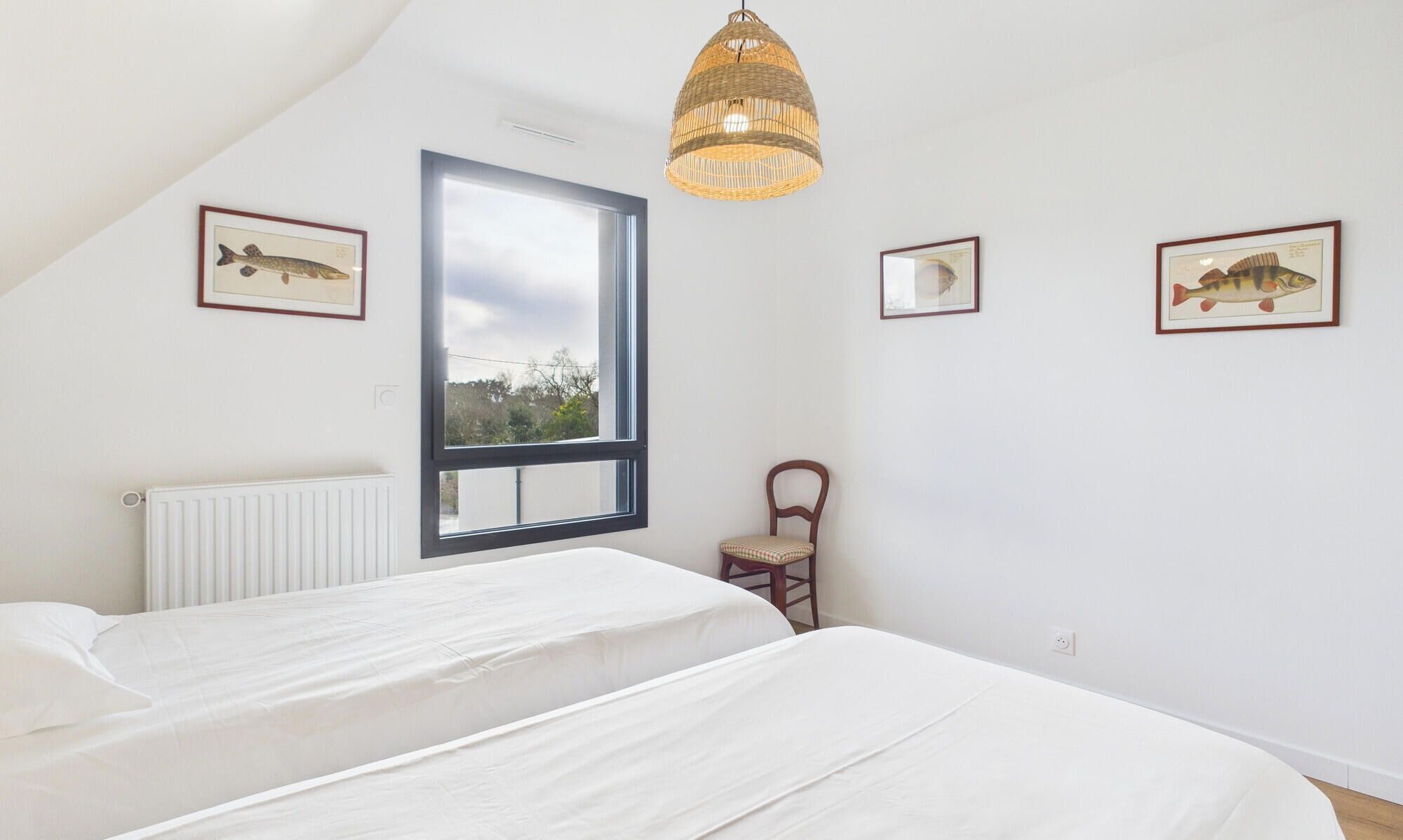 Une chambre avec deux lits, une grande fenêtre, une chaise et des tableaux représentant des poissons, accrochés aux murs.