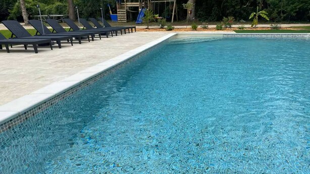 A swimming pool with clear blue water, surrounded by lounge chairs and a children's play area. - Charming French Countryside Escape with Pool (Barry d'Islemade)