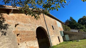 A brick building with a large arched entrance, surrounded by a grassy area and trees. - Charming French Countryside Escape with Pool (Barry d'Islemade)