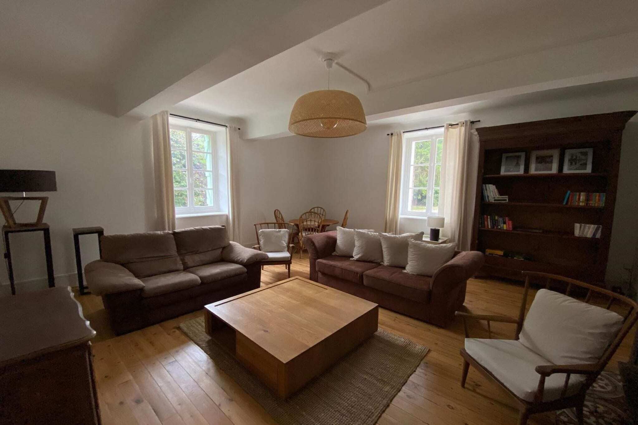 Una sala de estar con sofá, dos sillones, una mesa de centro, estantería e iluminación colgante.