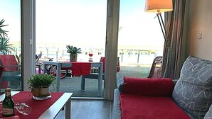 A room with a sofa, a table, and a view of the outside. There is a lamp and a plant on the table. - Coastal Apartment with Balcony (Fehmarn OT Burgtiefe-Südstrand)