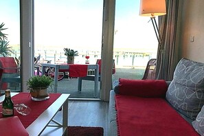 A room with a sofa, a table, and a view of the outside. There is a lamp and a plant on the table. - Coastal Apartment with Balcony (Fehmarn OT Burgtiefe-Südstrand)