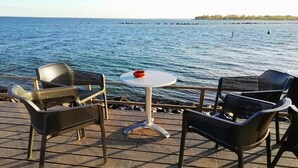 A deck with four wicker chairs and a small round table, overlooking a calm sea with boats in the distance. - Coastal Apartment with Balcony (Fehmarn OT Burgtiefe-Südstrand)