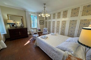 A bedroom with a large bed, a dresser, a chair, a table, and a chandelier. - A Place to Dream – Your Perfect Tuscan Home (Fucecchio)