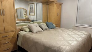 Un dormitorio con cama, armario, espejo y ventana con persianas.