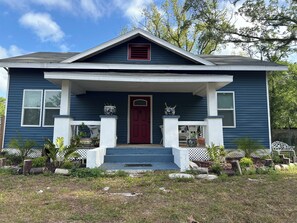 A two-story house with a red front door, white porch columns, and a small front yard with potted plants. - Delightful 2-bedroom house with AC in sunny Tampa (Tampa)