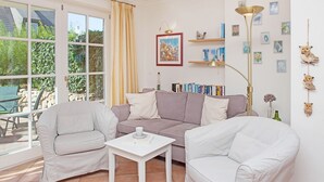 Una sala de estar con dos sillones blancos, un sofá gris, una mesa de centro blanca y una estantería con libros y adornos.
