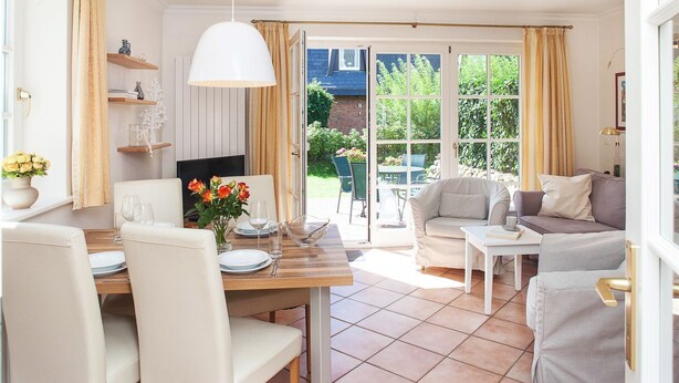 Una habitación luminosa y soleada con una mesa de comedor preparada para dos personas, un sofá y una televisión.