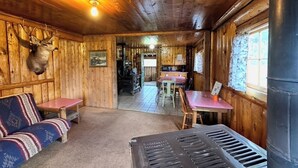 Een vakantiehuisje met houten plafond, een bank, een eettafel en een keukenhoek.