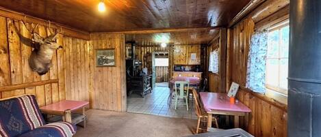 A cabin interior with a wooden ceiling, a sofa, a dining table, and a kitchen area.