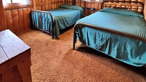 Een blokhut met twee bedden, een houten vloer en een raam met gordijnen.