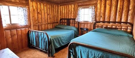 A cabin with two beds, a wooden floor, and a window with curtains.