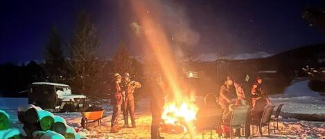 A group of people gathered around a campfire in a snowy outdoor setting.