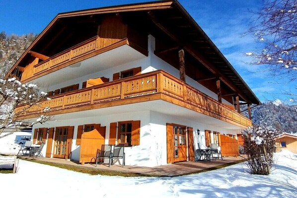 A two-story wooden chalet with balconies, a covered porch, and a snow-covered landscape.