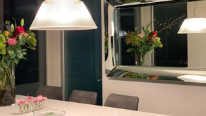 A modern dining area with a white table, chairs, and a large window with a view of greenery. - The Sweet Escape – Premium villa with pool (Theux)