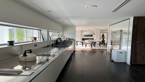 A modern kitchen with a long countertop, a kettle, and a sink. There is a dining area with a table and chairs in the background. - The Sweet Escape – Premium villa with pool (Theux)