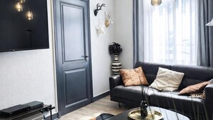 Ein modernes Wohnzimmer mit einem dunkelgrauen Sofa, einem wandmontierten Flachbildfernseher, Wanddekoration und einem großen Fenster mit Vorhängen.