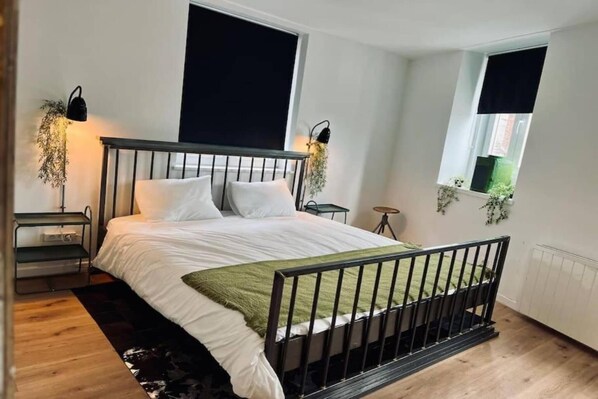 Un dormitorio con cama, mesitas de noche, ventana y radiador.