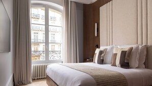 A hotel room with a large bed, a view of buildings, a radiator, and a window with curtains. - Luxury A/C Apt - 10P/4BDR - Arc de Triomphe (Paris)