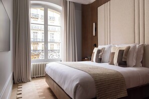 A hotel room with a large bed, a view of buildings, a radiator, and a window with curtains. - Luxury A/C Apt - 10P/4BDR - Arc de Triomphe (Paris)