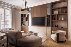 A modern living room with a sofa, a TV, and a wooden bookshelf. - Luxury A/C Apt - 10P/4BDR - Arc de Triomphe (Paris)