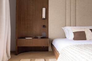 A neatly arranged bedroom with a wooden nightstand, a bedside table, a bed with white and brown bedding, and a wall-mounted lamp. - Luxury A/C Apt - 10P/4BDR - Arc de Triomphe (Paris)