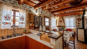Una cocina rústica con vigas de madera, paredes de piedra y una isla central con un lavamanos y diversos utensilios de cocina.