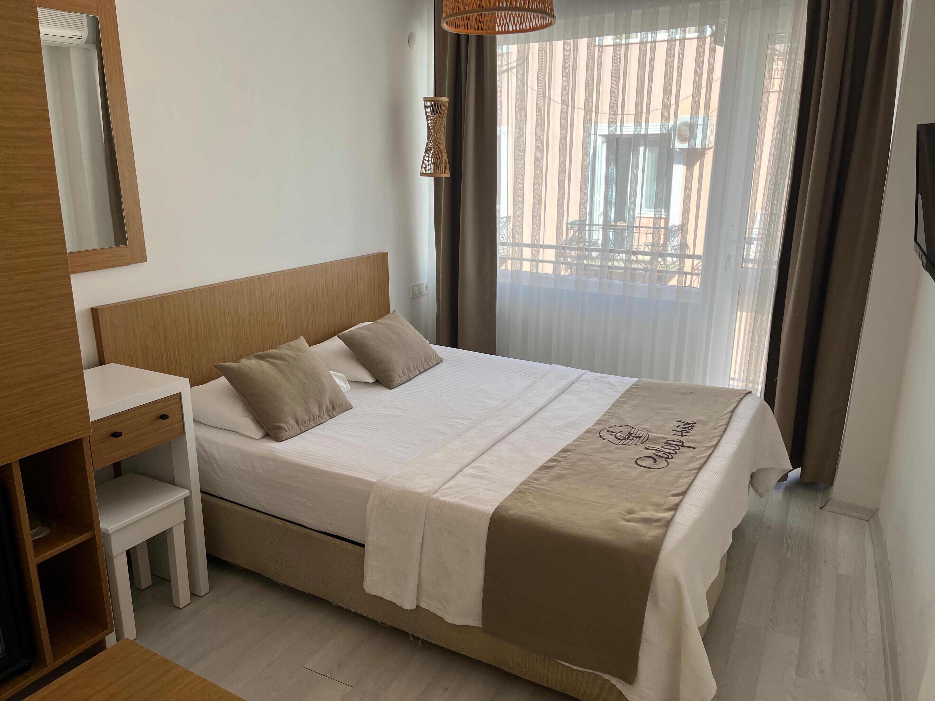 Habitación de hotel ordenada con cama, mesita de noche, espejo y vista al balcón exterior.