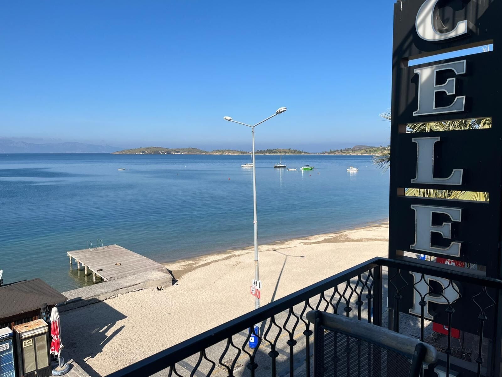 A beach view with a clear sky, a wooden pier, and a sign with the letters 'C E L E'.