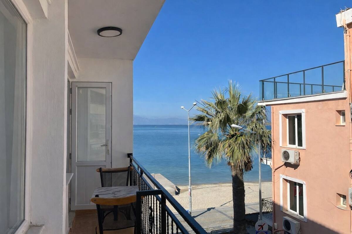Un balcón con vista al mar, una palmera y un edificio con ventana y unidad de aire acondicionado.