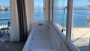 Een kamer met een badkuip, grote ramen en uitzicht op zee.