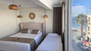 Een hotelkamer met twee bedden, een groot raam met uitzicht op het strand en gebouwen, en een plafond met een decoratieve spiegel.
