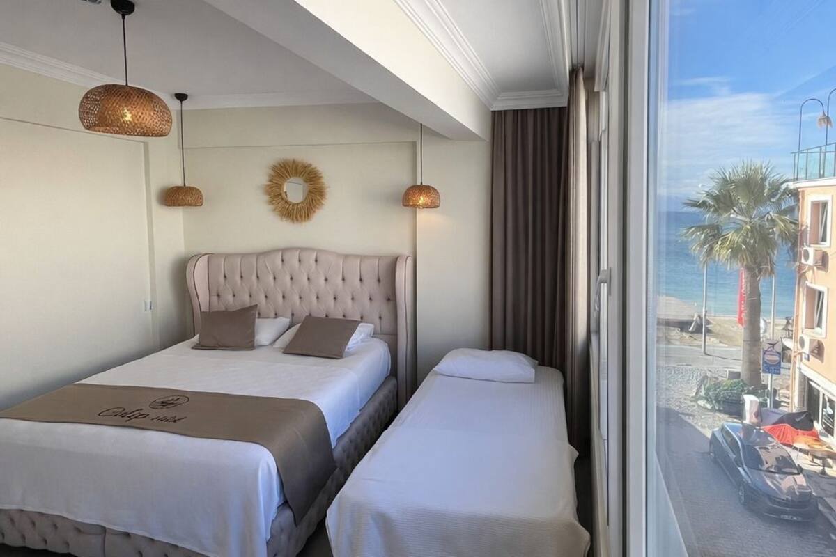 Habitación de hotel con dos camas, un ventanal con vistas a la playa y edificios, y un techo con un espejo decorativo.