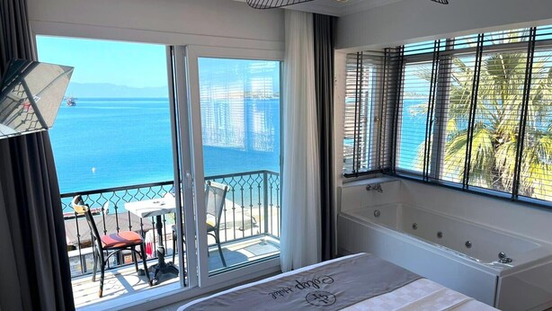 Een hotelkamer met balkon, een bed, een badkuip en uitzicht op zee.
