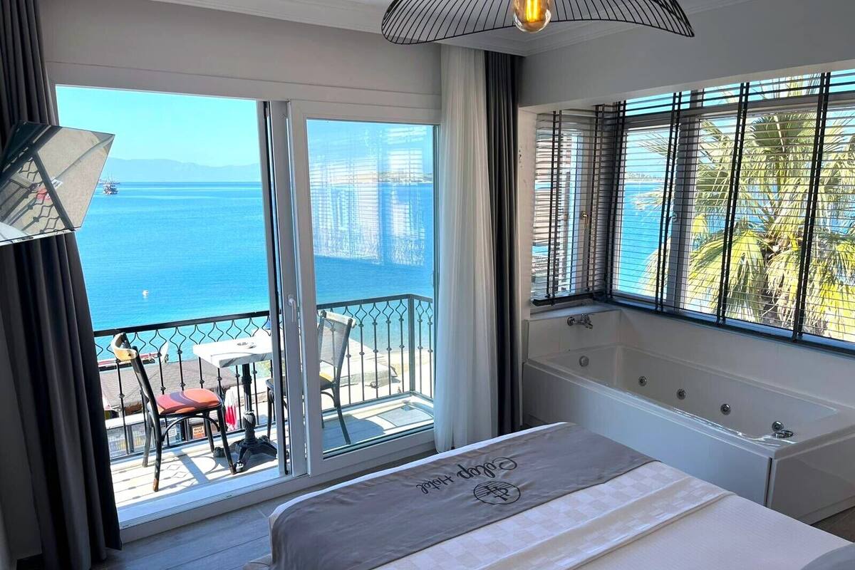 Habitación de hotel con balcón, cama, bañera y vista al mar.