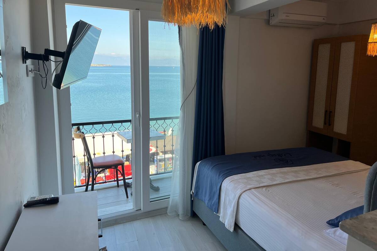 Un dormitorio con cama, televisor, balcón con vista al mar y ventilador de techo.