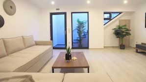 A modern living room with a sofa, a coffee table with a plant, and a staircase leading to an upper level. - Stone Crafted Luxury Villas - Villa Artemis (Nikiana)