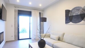 A modern living room with a sofa, a coffee table with a vase, a flat-screen TV, and a painting on the wall. - Stone Crafted Luxury Villas - Villa Artemis (Nikiana)