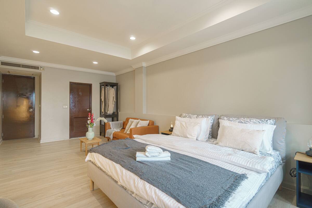 A spacious bedroom with a large bed, a sitting area with a sofa, and a small table with a vase of flowers.